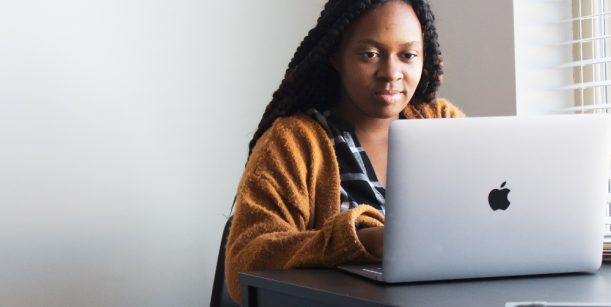 person wearing orange jumper typing on mac laptop