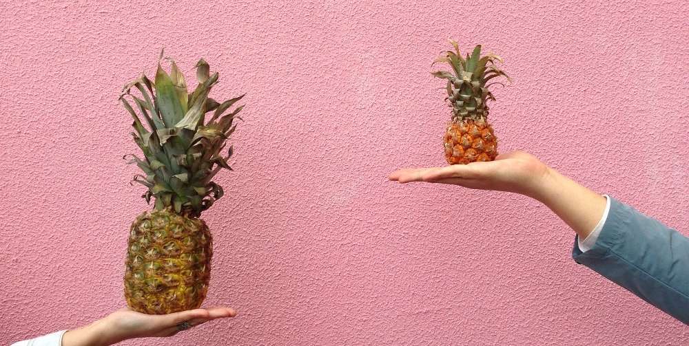 two people holding a pineapple on a pink background