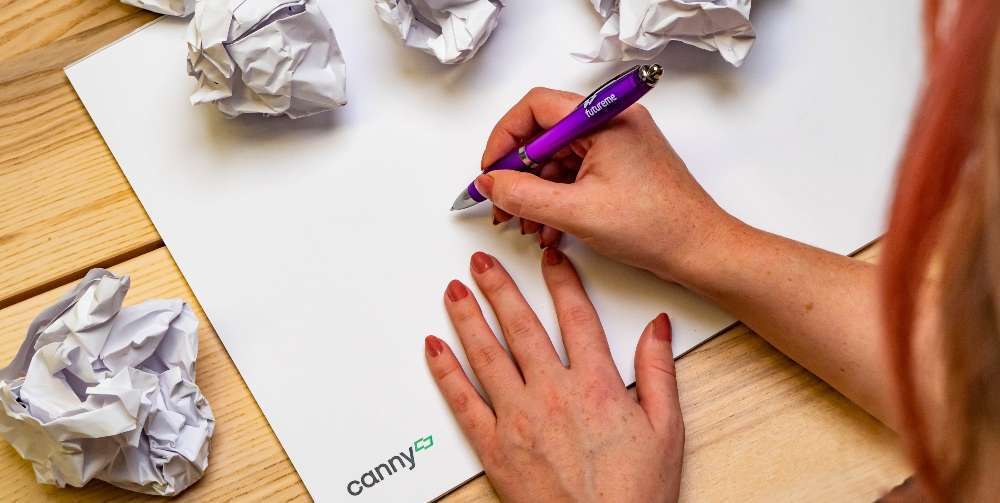 person writing on notepad with crumpled paper around