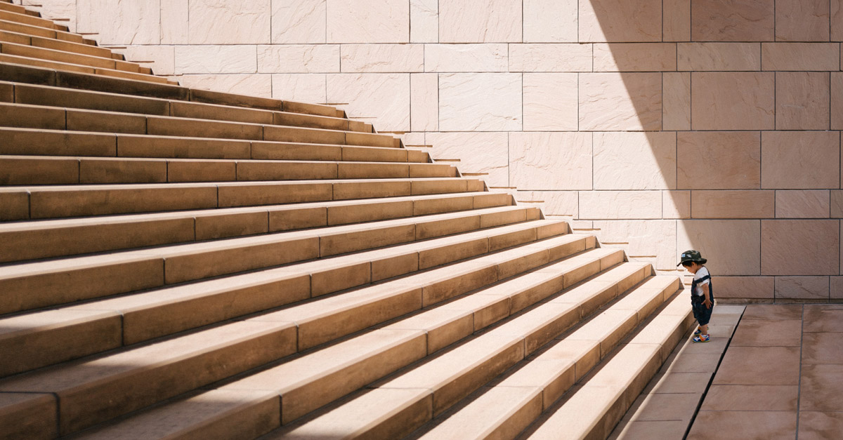 A small child looking at a monumental set of stairs representing a challenge