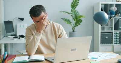 A man with his head in his hands in front of a laptop